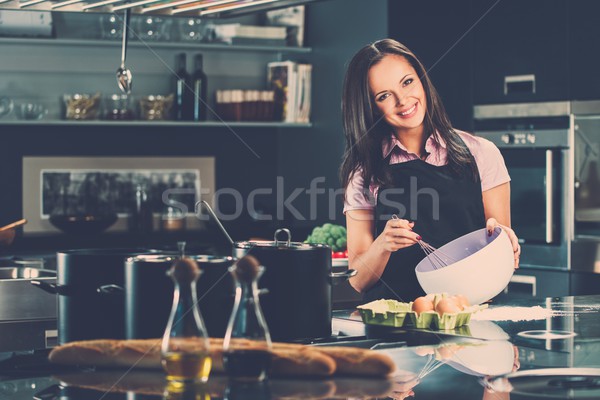 Young woman in apron whisking eggs for a dough on a modern kitchen Stock photo © Nejron