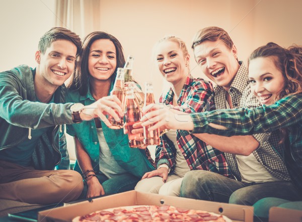 Group of young multi-ethnic friends with pizza and bottles of drink celebrating in home interior Stock photo © Nejron