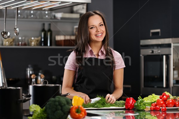Stock photo: Happy young woman in apron on modern kitchen cutting vegetables