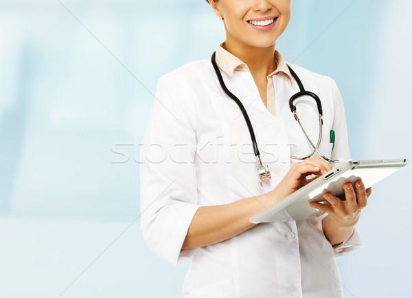 Young positive brunette doctor woman taking notes on tablet pc  Stock photo © Nejron