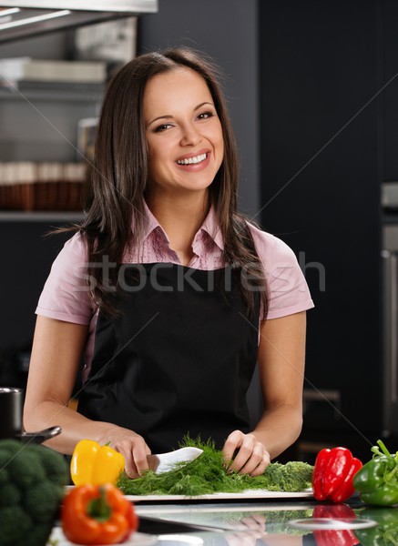 Happy young woman in apron on modern kitchen cutting vegetables Stock photo © Nejron