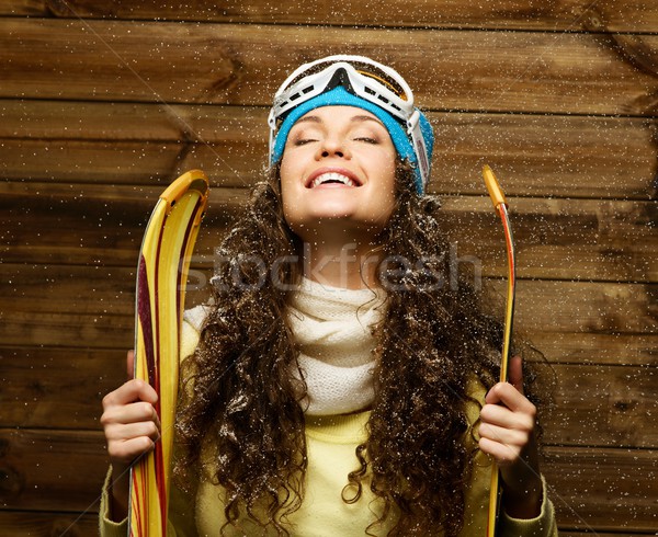 Stock photo: Smiling woman with skies standing against wooden house wall under snow