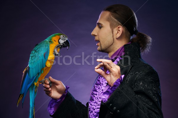 Young handsome brunette magician man in stage costume with his trained parrot Stock photo © Nejron