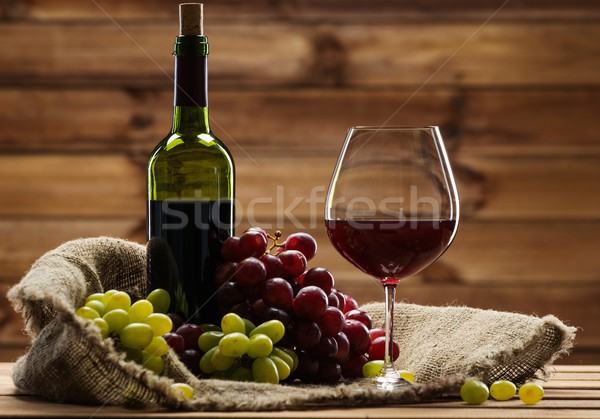 Bottle of red wine, glass and grape on a sack in wooden interior  Stock photo © Nejron