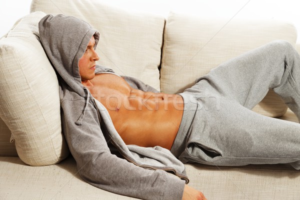 Sporty man in grey hoodie with muscular torso relaxing on sofa Stock photo © Nejron