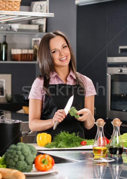 Happy young woman in apron on modern kitchen cutting vegetables Stock photo © Nejron