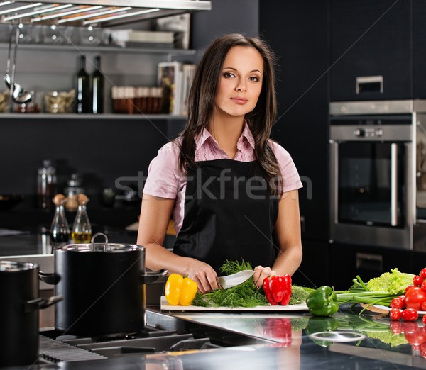 Cheerful young woman in apron on modern kitchen cutting vegetables Stock photo © Nejron