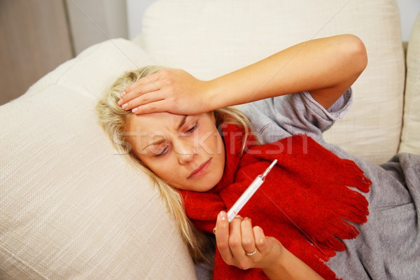 Sick young woman with thermometer lying on sofa at home Stock photo © Nejron