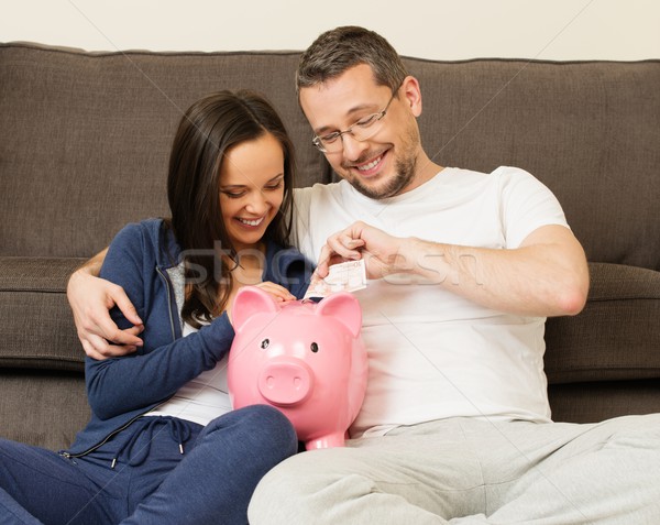 Cheerful young couple putting banknote in piggybank  Stock photo © Nejron