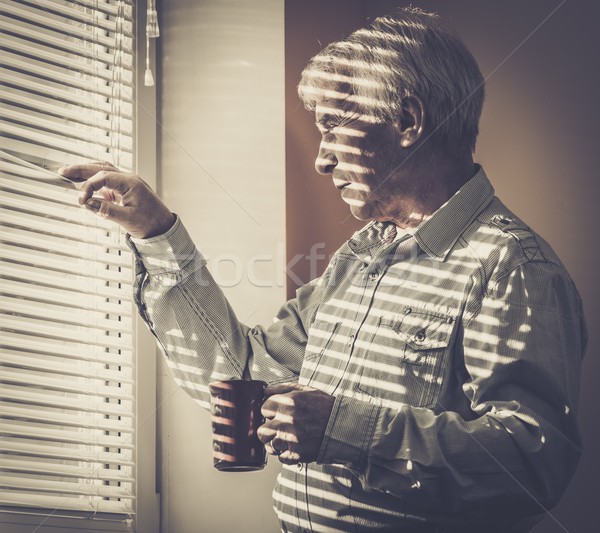 Senior man with cup looking out the window through jalousie  Stock photo © Nejron