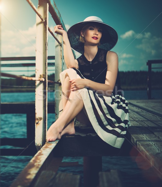 Beautiful woman wearing hat and white scarf sitting on old wooden pier  Stock photo © Nejron