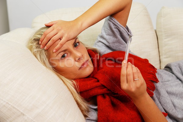 Sick young woman with thermometer lying on sofa at home Stock photo © Nejron
