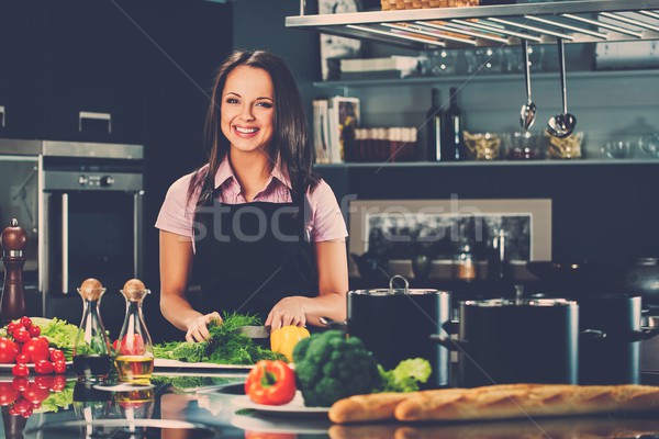 Cheerful young woman in apron on modern kitchen cutting vegetables Stock photo © Nejron