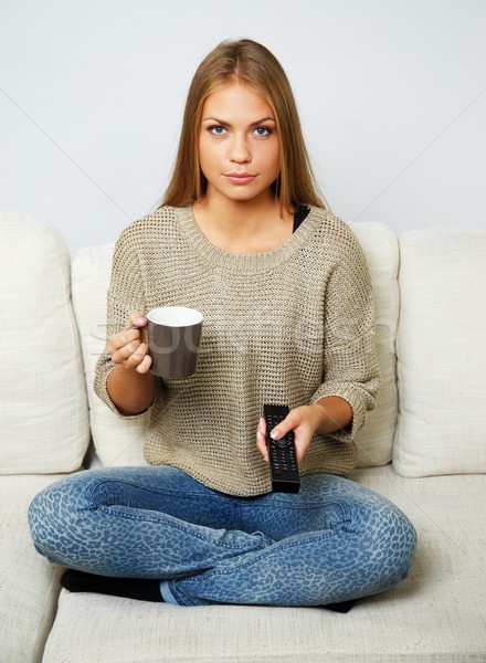 Stock photo: Young beautiful woman on a sofa with remote control and mug