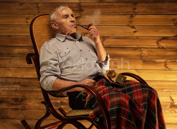 Senior man with smoking pipe sitting on rocking chair in homely wooden interior Stock photo © Nejron