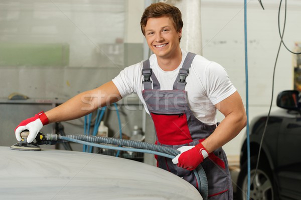Young serviceman performing grinding with machine on a car bonnet in a workshop Stock photo © Nejron