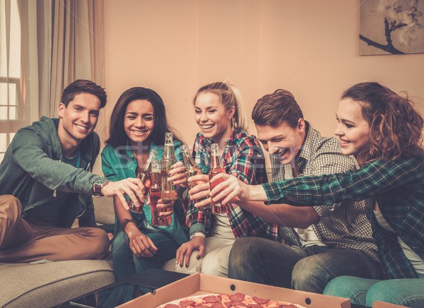 Stock photo: Group of young multi-ethnic friends with pizza and bottles of drink celebrating in home interior