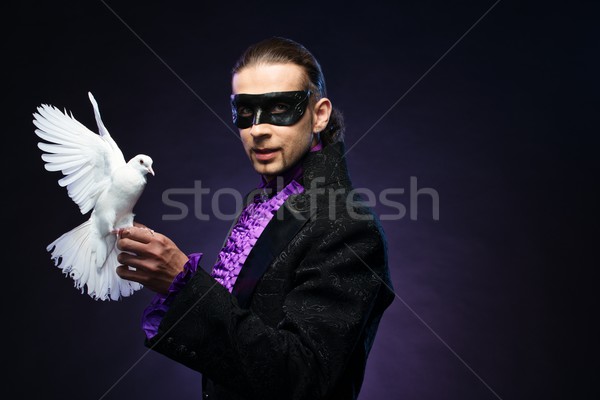 Young handsome brunette magician man in stage costume with his trained white dove Stock photo © Nejron