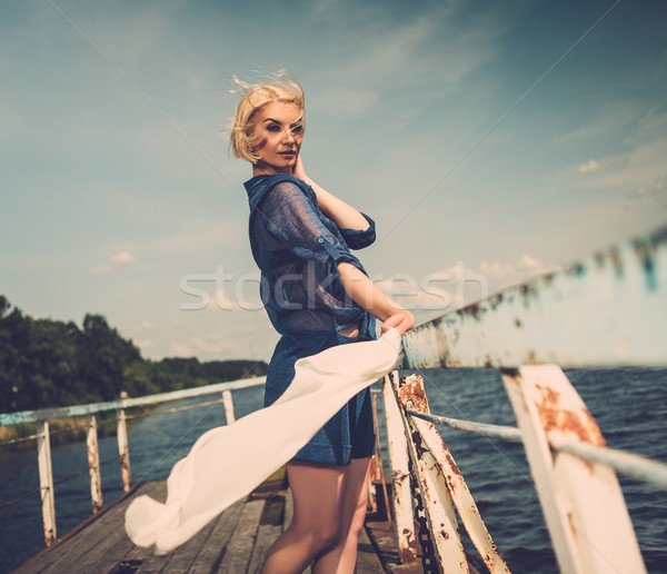 Stylish beautiful blond woman with white scarf standing near rails of old pier Stock photo © Nejron