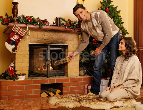 Stock photo: Couple putting log into  fireplace in Christmas decorated house interior 