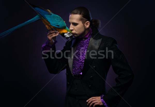 Young handsome brunette magician man in stage costume with his trained parrot Stock photo © Nejron