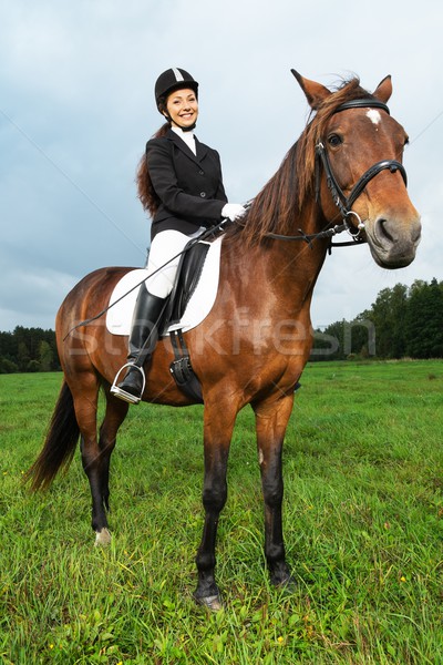 Stock photo: Cheerful young woman ridding horse in a field 