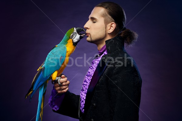 Stock photo: Young handsome brunette magician man in stage costume with his trained parrot