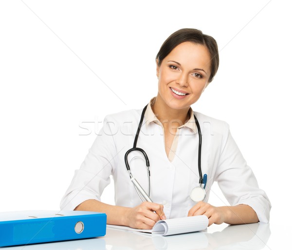 Young positive brunette doctor woman behind table taking notes Stock photo © Nejron