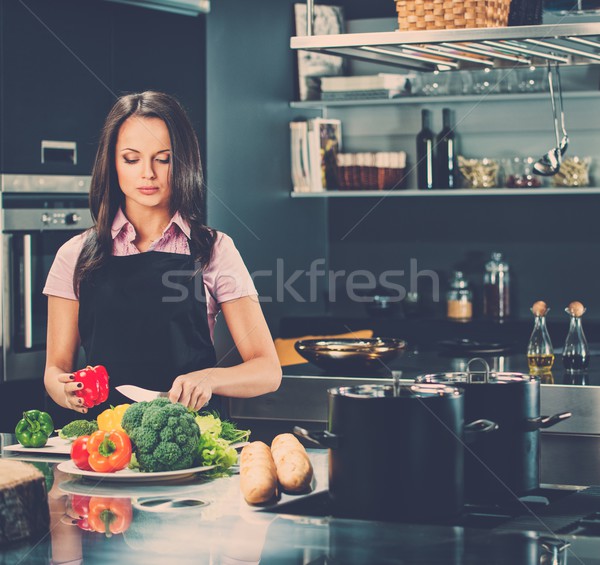 Cheerful young woman in apron on modern kitchen cutting vegetables Stock photo © Nejron