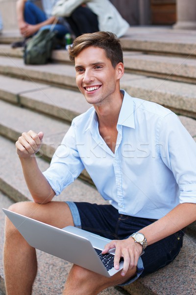 Stock photo: Handsome young man with laptop sitting on a steps outdoors