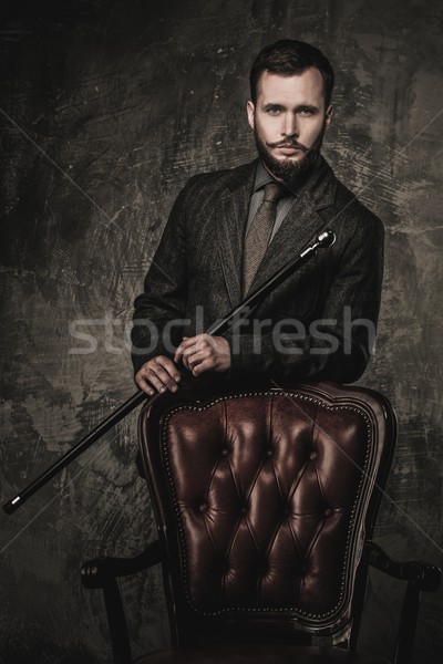 Handsome well-dressed man with stick standing near leather chair  Stock photo © Nejron
