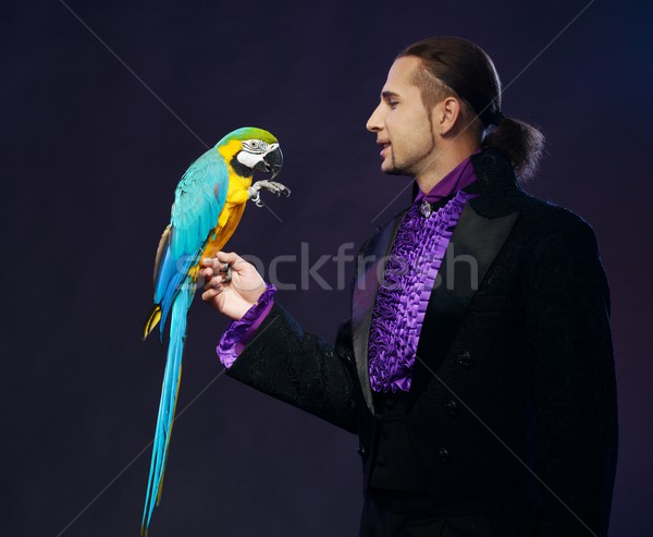 Young handsome brunette magician man in stage costume with his trained parrot Stock photo © Nejron