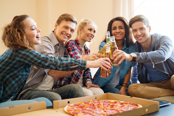 Group of young multi ethnic friends with pizza and bottles of drink celebrating in home interior Stock photo © Nejron