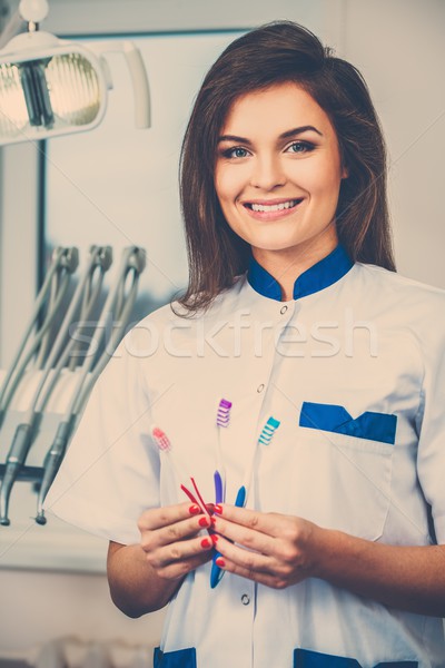 Young beautiful brunette female dentist with three toothbrushes at dentist's surgery  Stock photo © Nejron