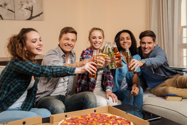 Group of young multi-ethnic friends with pizza and bottles of drink celebrating in home interior Stock photo © Nejron