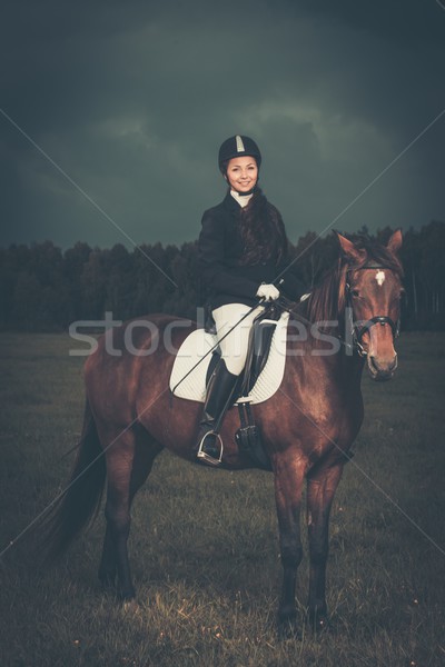 Beautiful girl sitting on a horse outdoors against moody sky Stock photo © Nejron