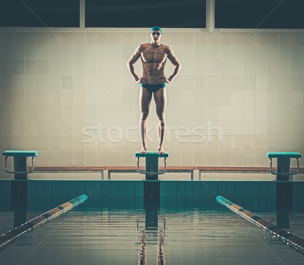 Young muscular swimmer standing on starting block in a swimming pool Stock photo © Nejron