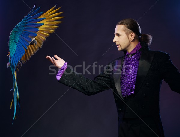 Young handsome brunette magician man in stage costume with his trained parrot Stock photo © Nejron