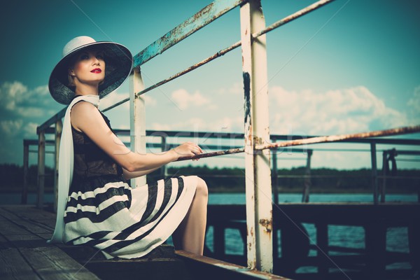 Beautiful woman wearing hat and white scarf sitting on old wooden pier  Stock photo © Nejron