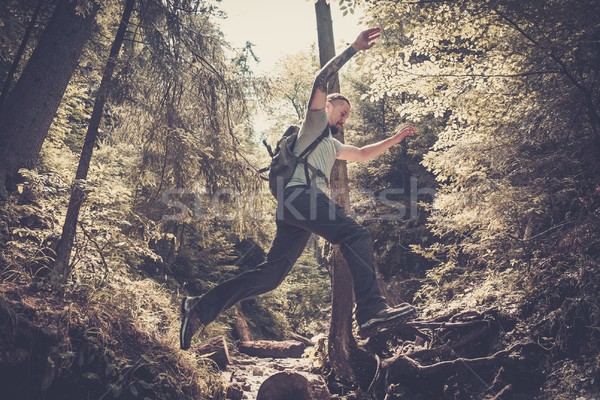 Man hiker jumping across stream in mountain forest Stock photo © Nejron