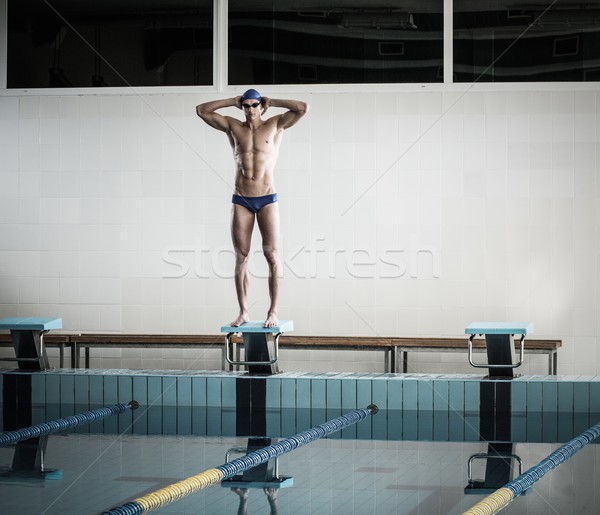 Young muscular swimmer standing on starting block in a swimming pool Stock photo © Nejron