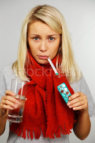 Sick young blond woman with pills, thermometer, and glass of water Stock photo © Nejron
