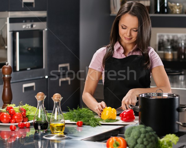 Cheerful young woman in apron on modern kitchen cutting vegetables Stock photo © Nejron