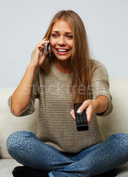 Young beautiful woman on a sofa with remote control and mobile pone Stock photo © Nejron