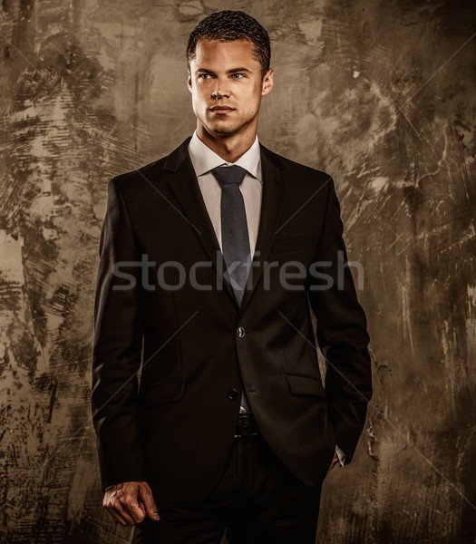 Stock photo: Well-dressed man in black suit against grunge wall 