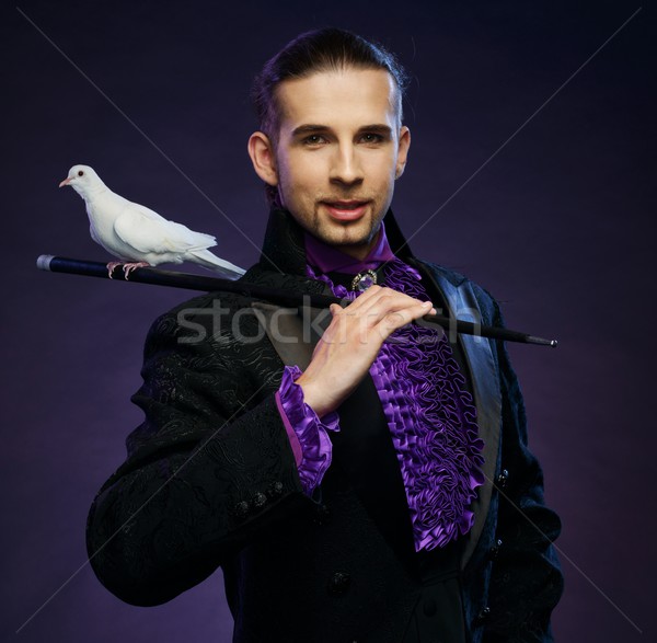 Stock photo: Young handsome brunette magician man in stage costume with his trained white doves