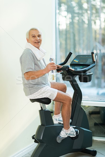 Senior man with bottle of water on a bike in a fitness club Stock photo © Nejron
