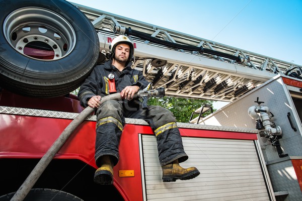 Firefighter sitting on a firefighting truck with water hose  Stock photo © Nejron