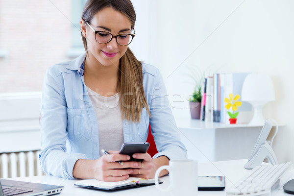 Pretty young woman using her mobile phone in the office. Stock photo © nenetus