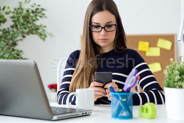 Stock photo: Confident young woman working in her office with mobile phone.